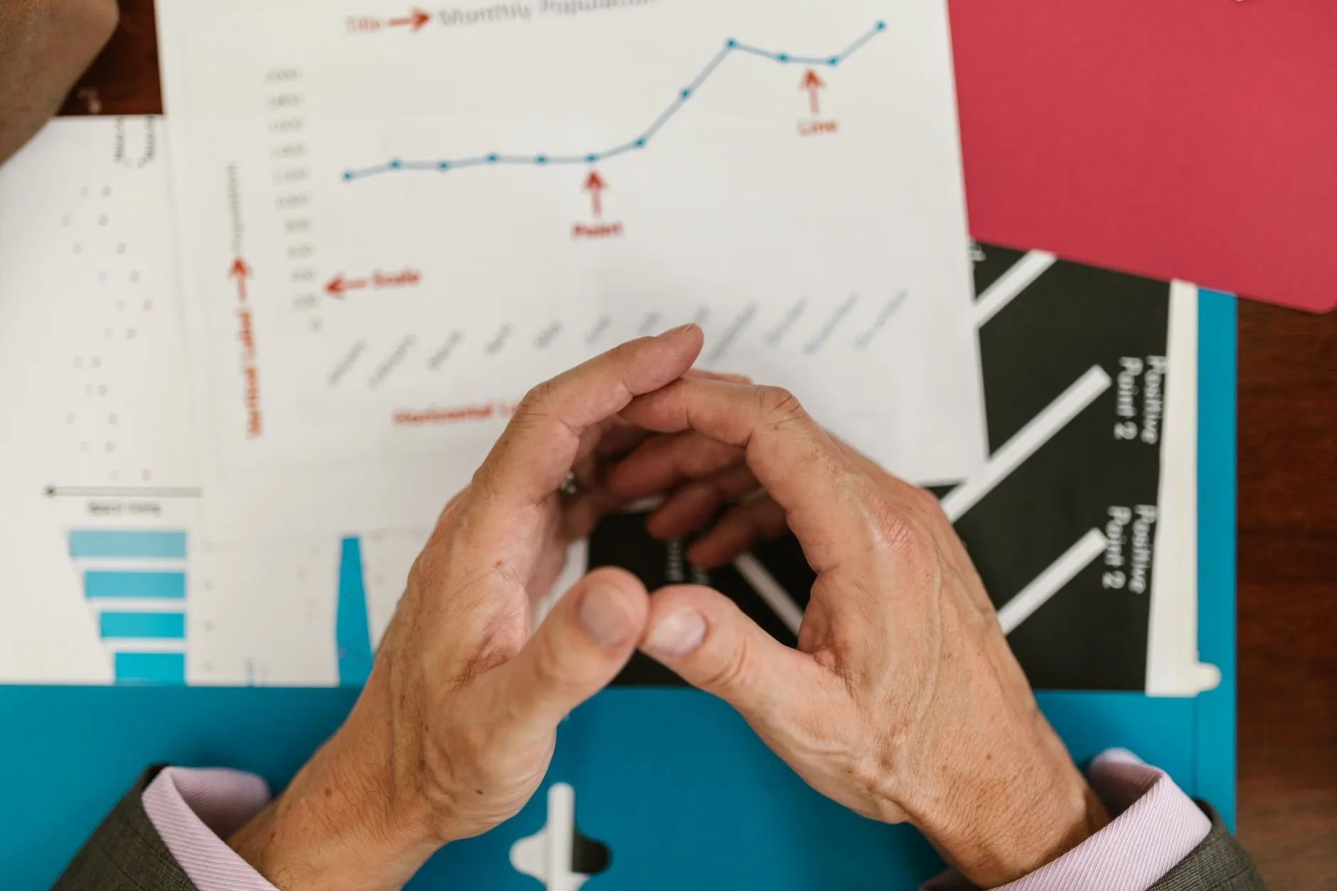 Clasped hands resting over printed line and bar charts on a blue folder, seen from above